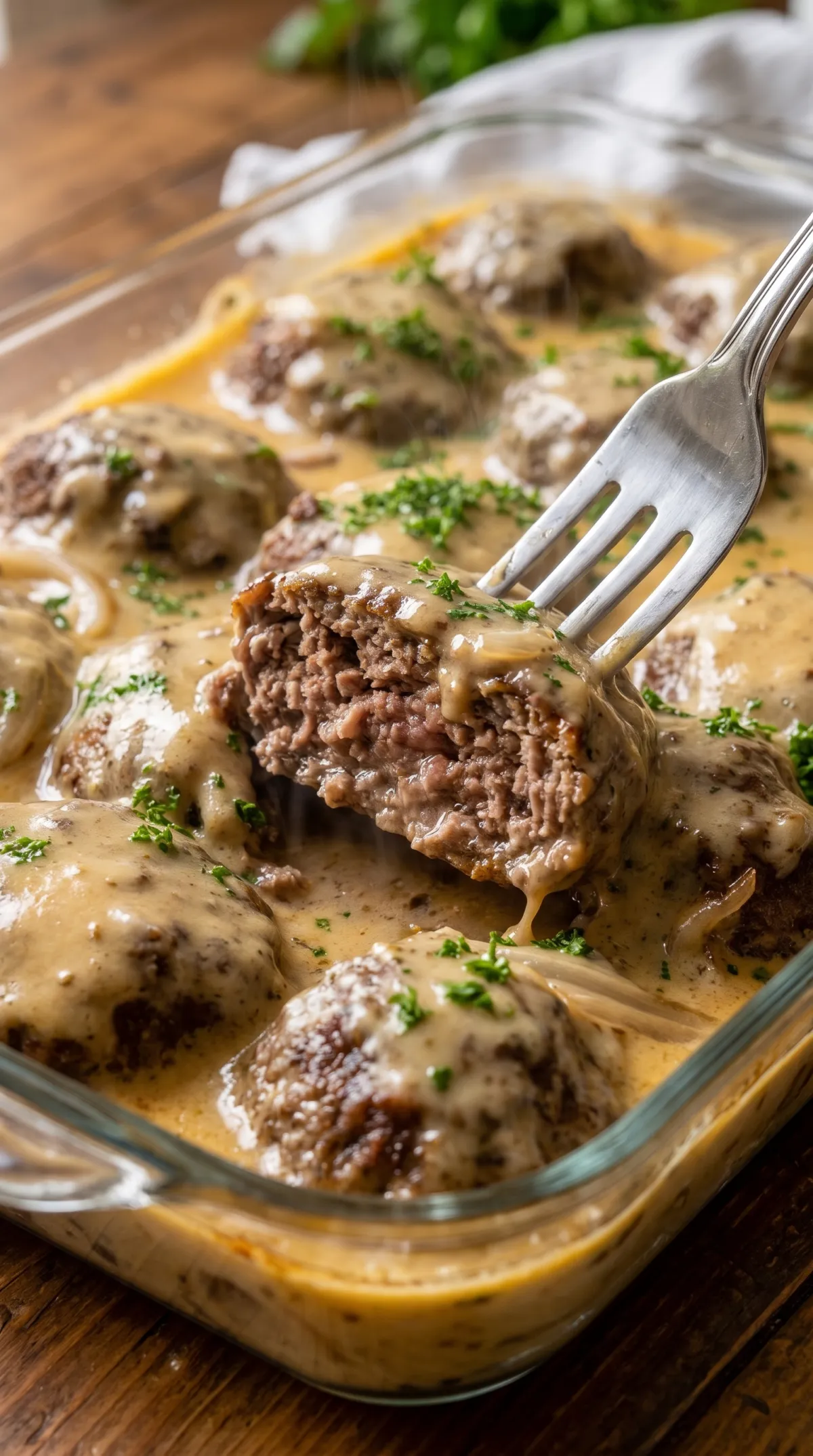 Fork cutting into a baked hamburger steak to show the juicy, tender beef under creamy mushroom gravy